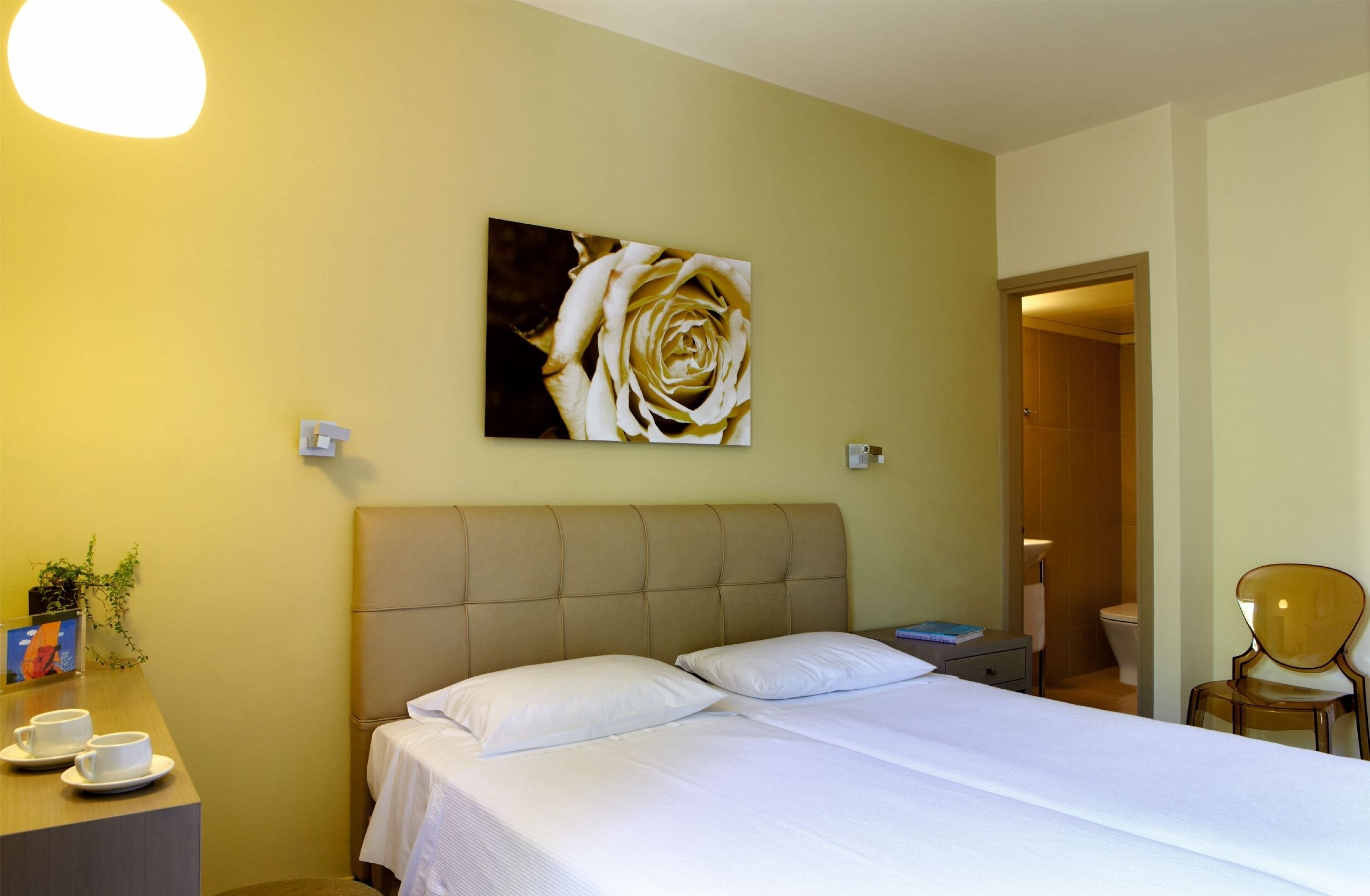 Una habitación de hotel con cama, mesita de noche y un cuadro de rosa colgado en la pared.