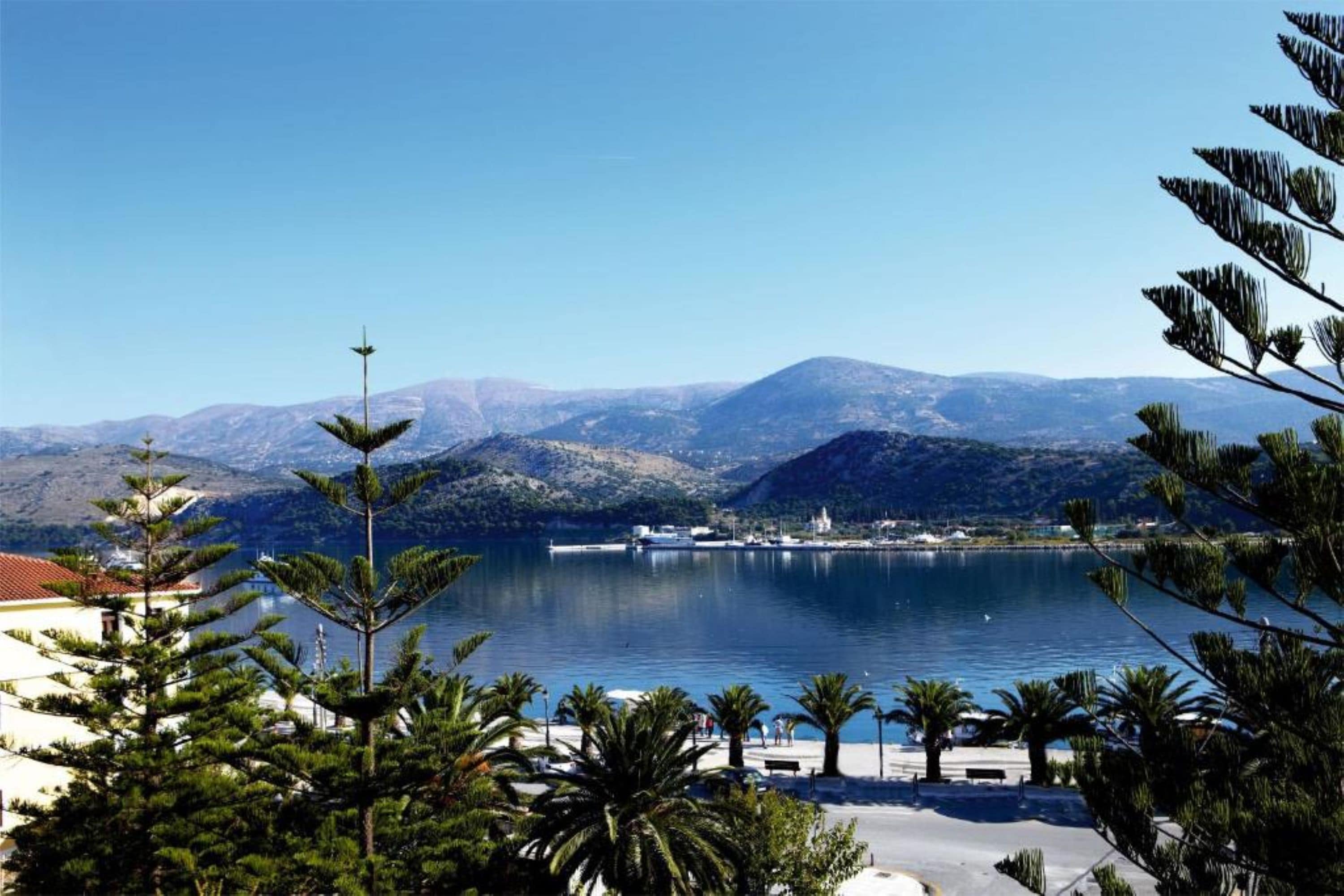 Vista costera con un puerto deportivo, montañas y cielo despejado.