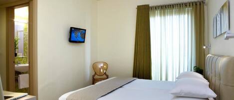 Une chambre d’hôtel avec un lit, un bureau avec un ordinateur portable, une chaise, un téléviseur fixé au mur et une fenêtre avec des rideaux.