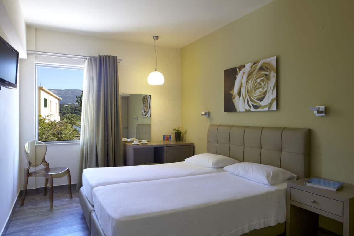 Hotelkamer met een bed, bureau, stoel, raam met gordijnen, een schilderij en uitzicht.