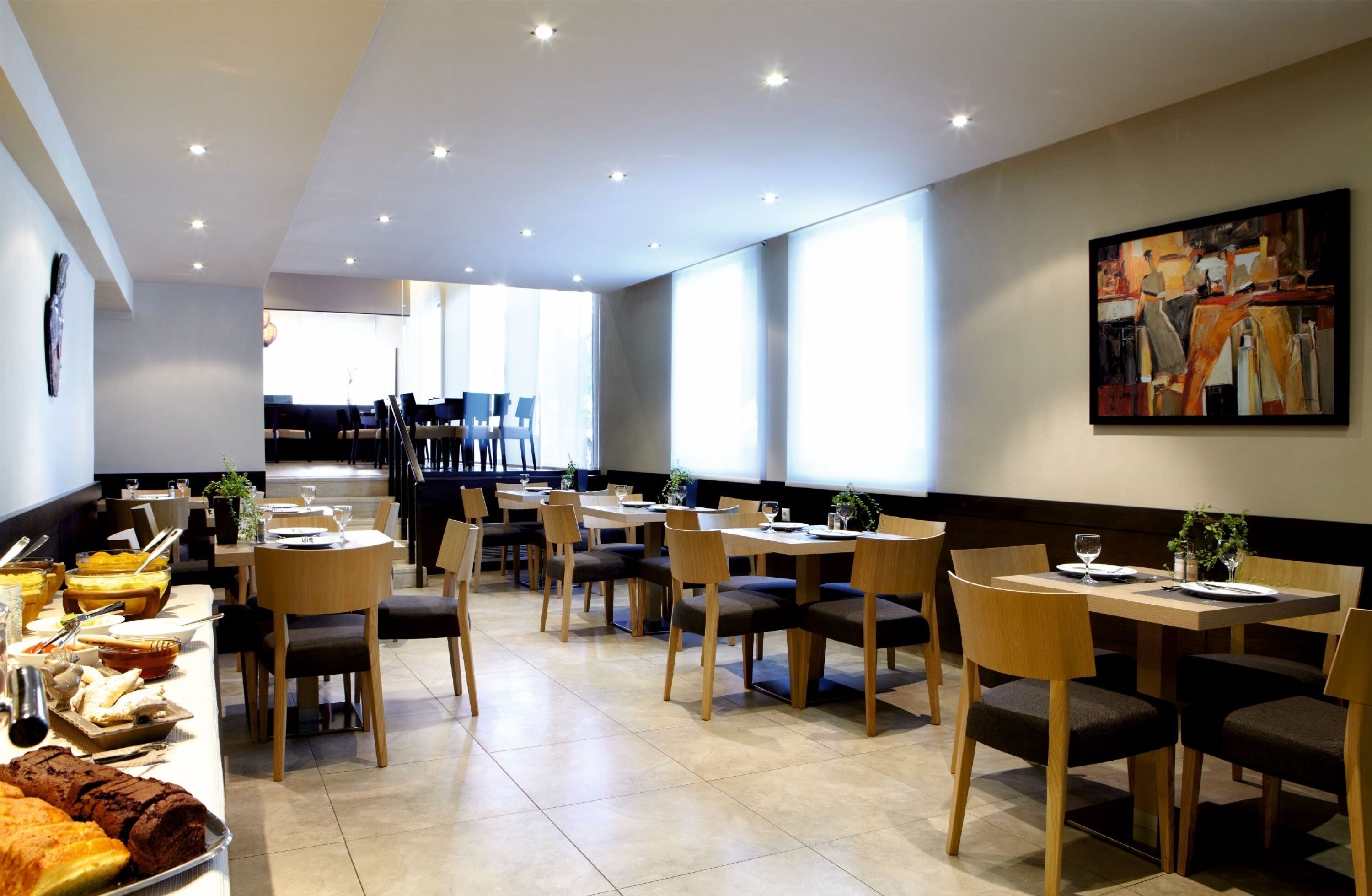 Ein moderner Essbereich mit mehreren Tischen und Stühlen, einem Buffet mit verschiedenen Speisen und einem Gemälde an der Wand.