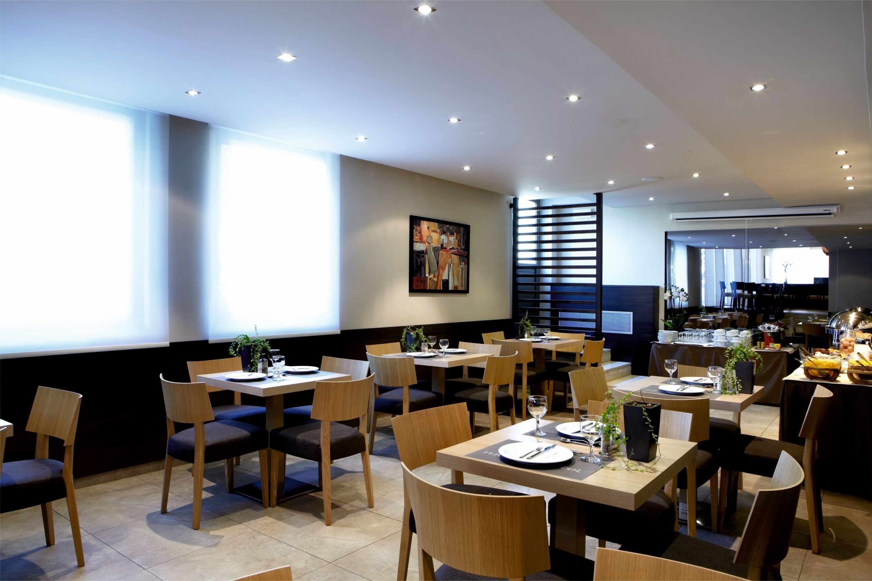 A modern restaurant with multiple dining tables and chairs, a large window, and an air conditioning unit visible in the background.