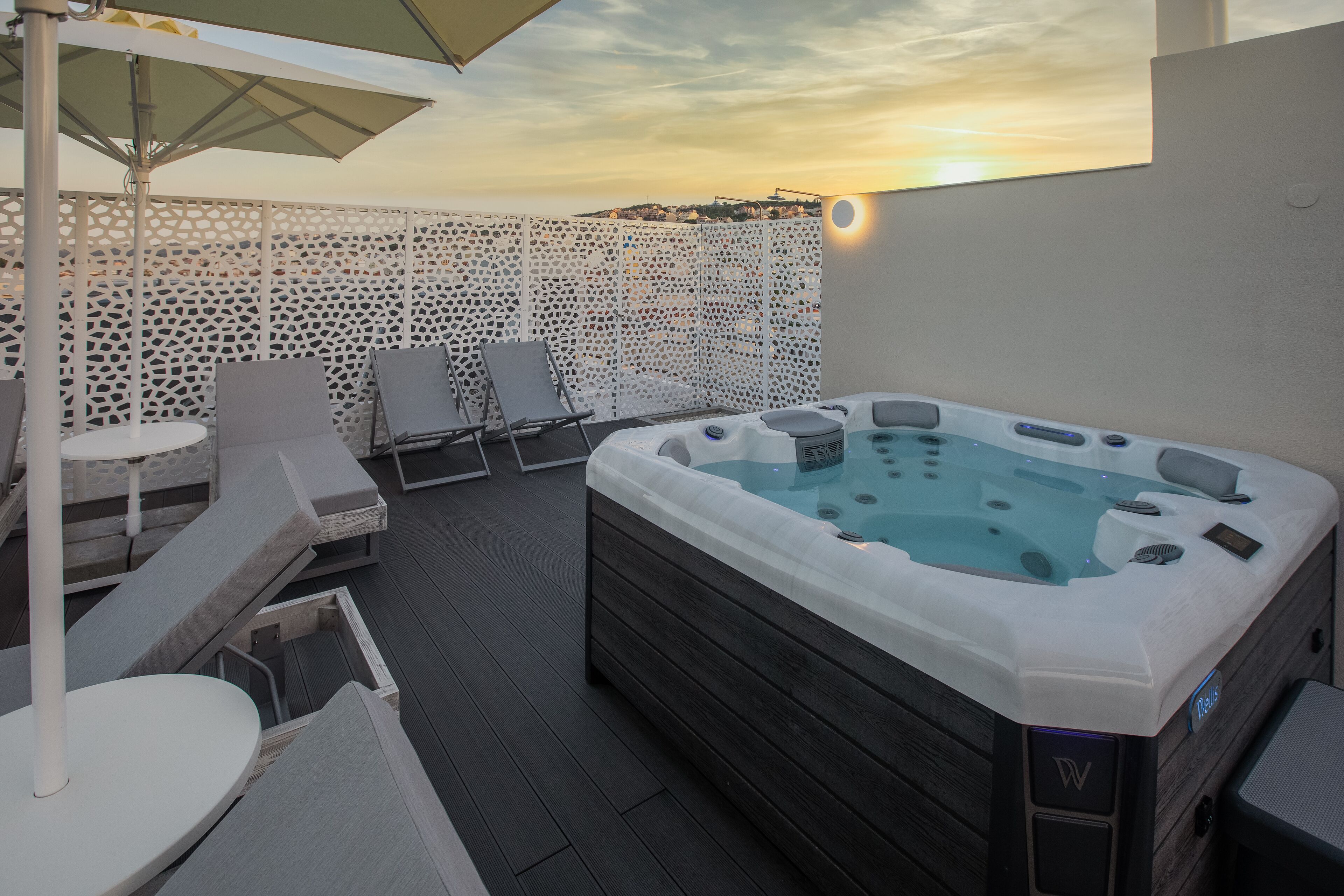 Una terraza en la azotea con jacuzzi, sillones de descanso y una mesa bajo una sombrilla.