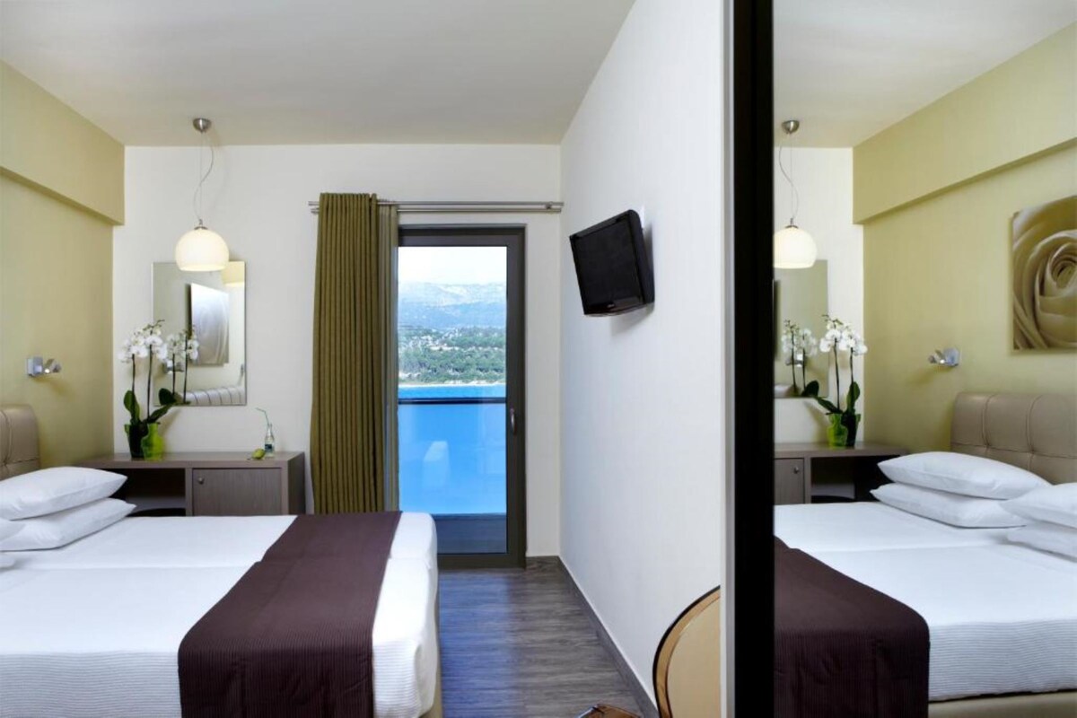 Ein Hotelzimmer mit zwei Betten, einem Fernseher, einem Balkon mit Blick und einem Spiegel.