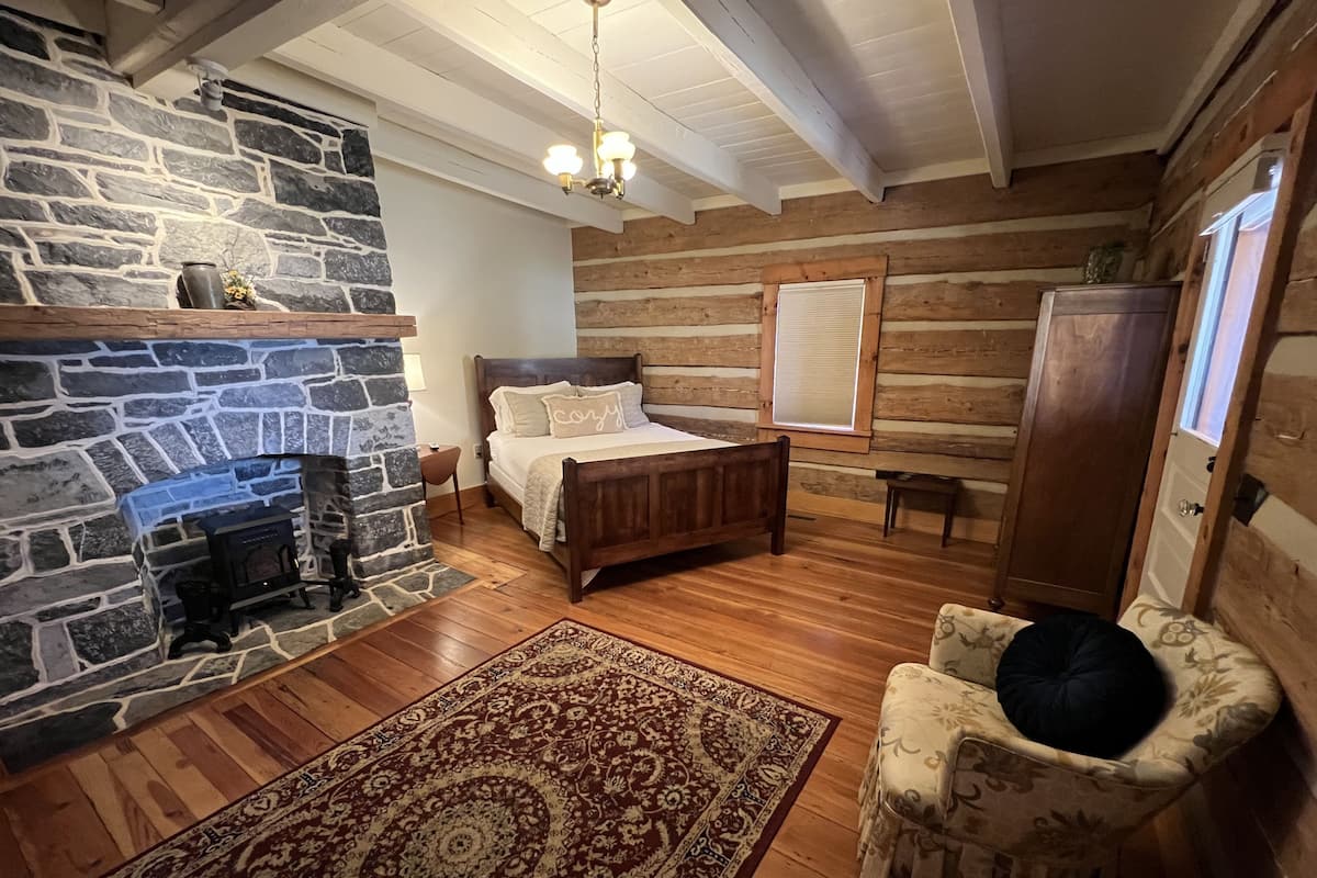 A log cabin bedroom with a stone fireplace, wooden bed, and a cozy chair.