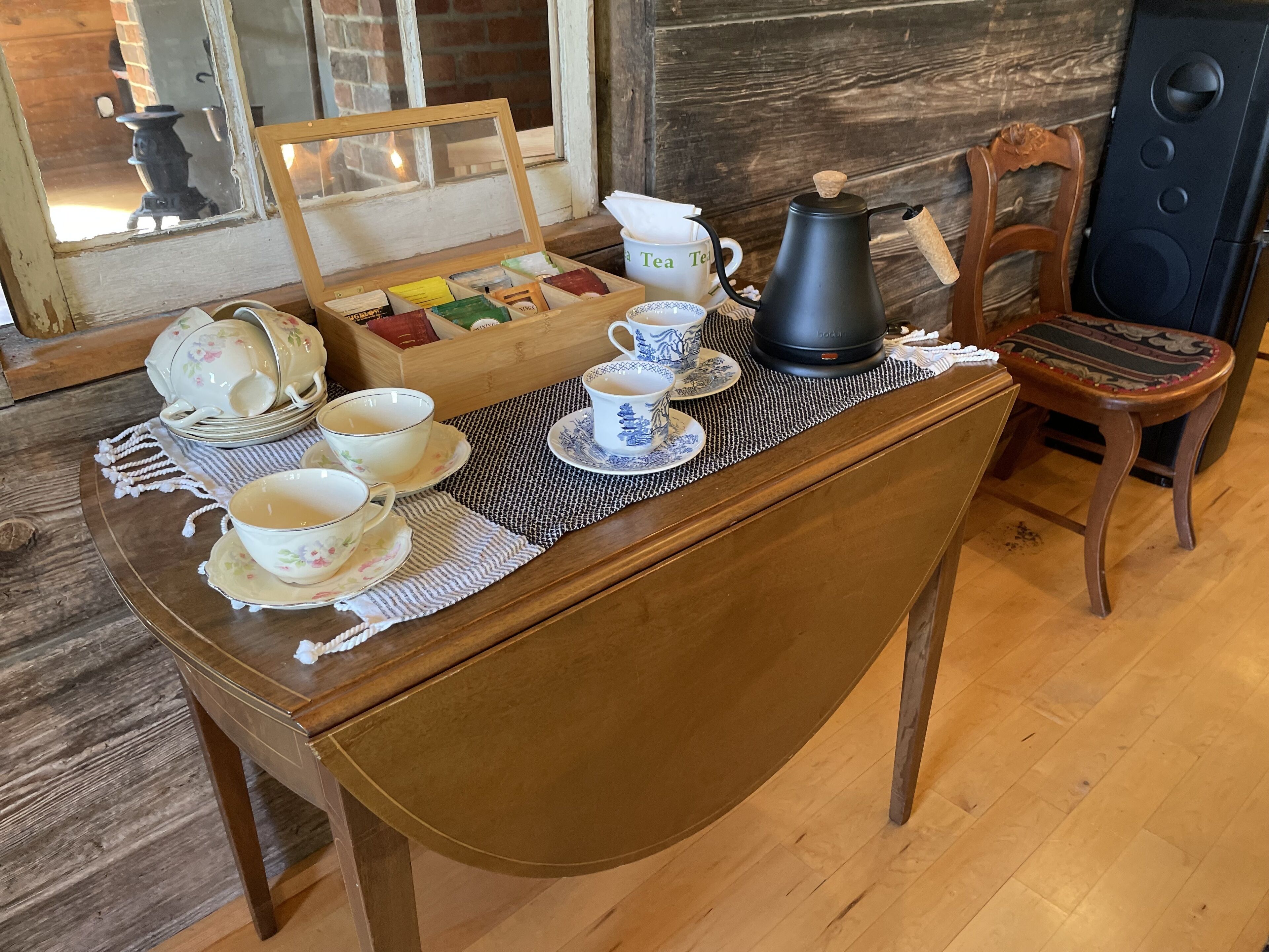 A wooden table with a tea set, including cups, saucers, and a teapot, set on a woven placemat.