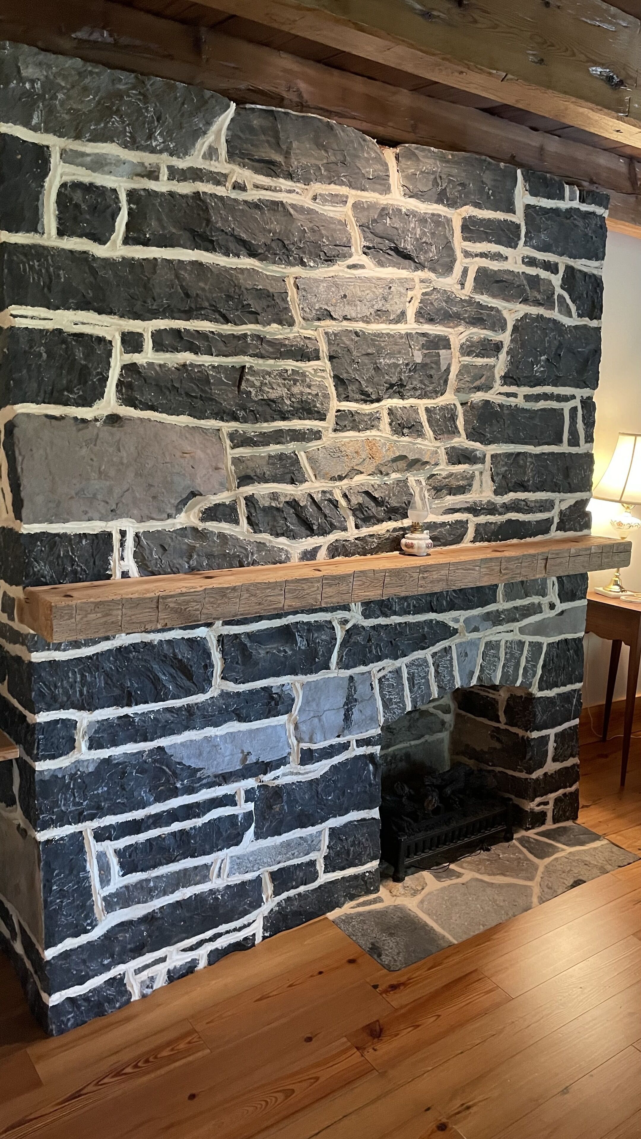 A stone fireplace with a wooden mantel and a small table beside it.