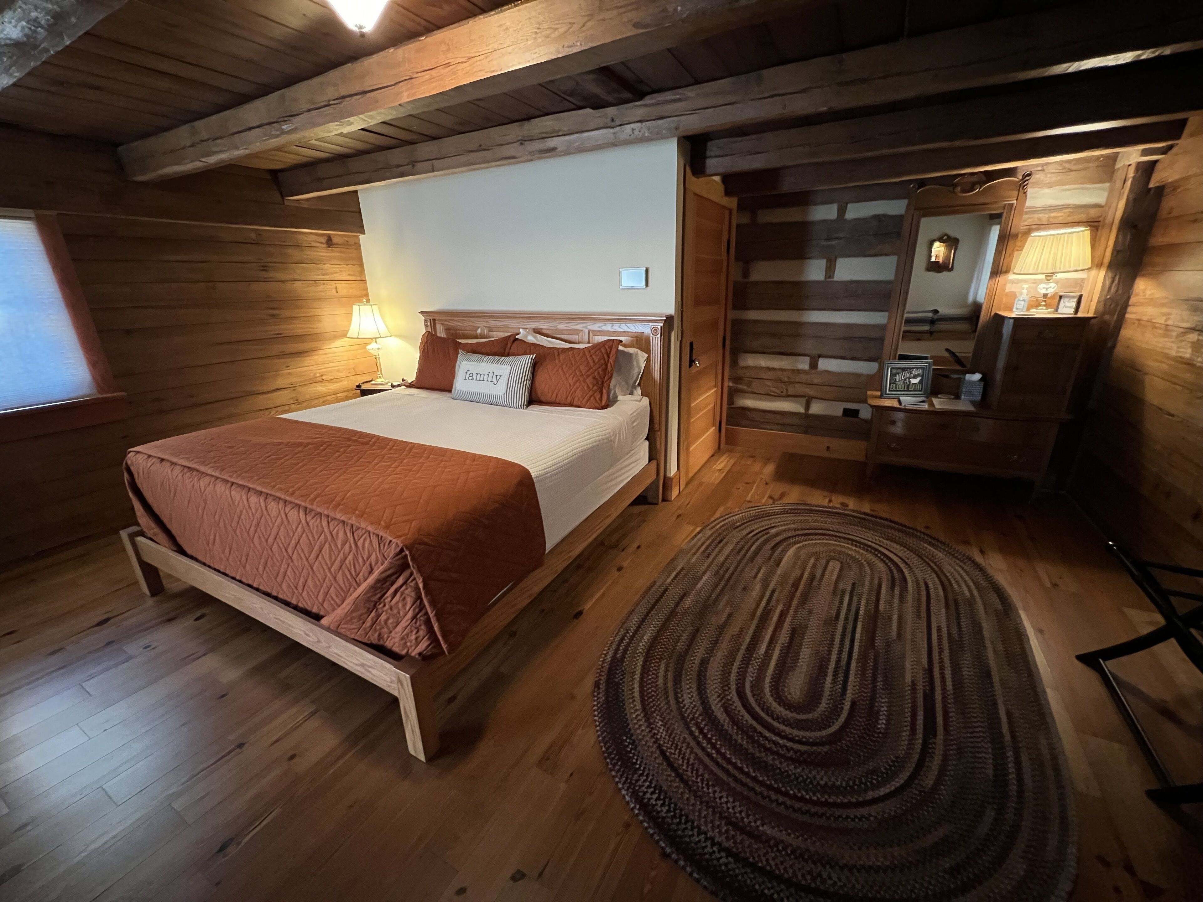 Un dormitorio de cabaña de madera con una cama, lámparas de noche, un espejo y una alfombra.