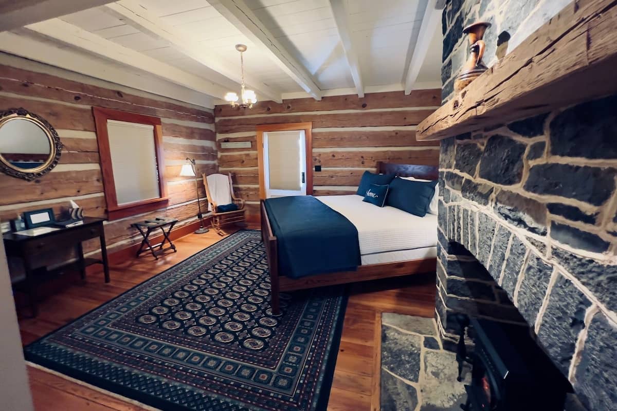 A log cabin bedroom with a stone fireplace, a bed with blue bedding, a desk, and a mirror.