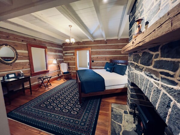 A log cabin bedroom with a stone fireplace, a bed with blue bedding, a desk, and a mirror. - Silver Lake Bed and Breakfast (Dayton)