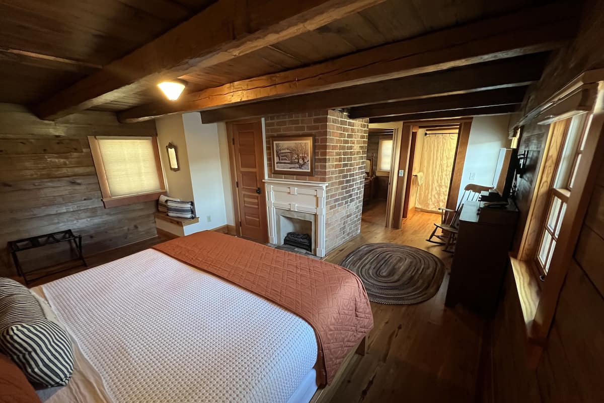 A cozy bedroom with a large bed, a fireplace, and a wooden ceiling.