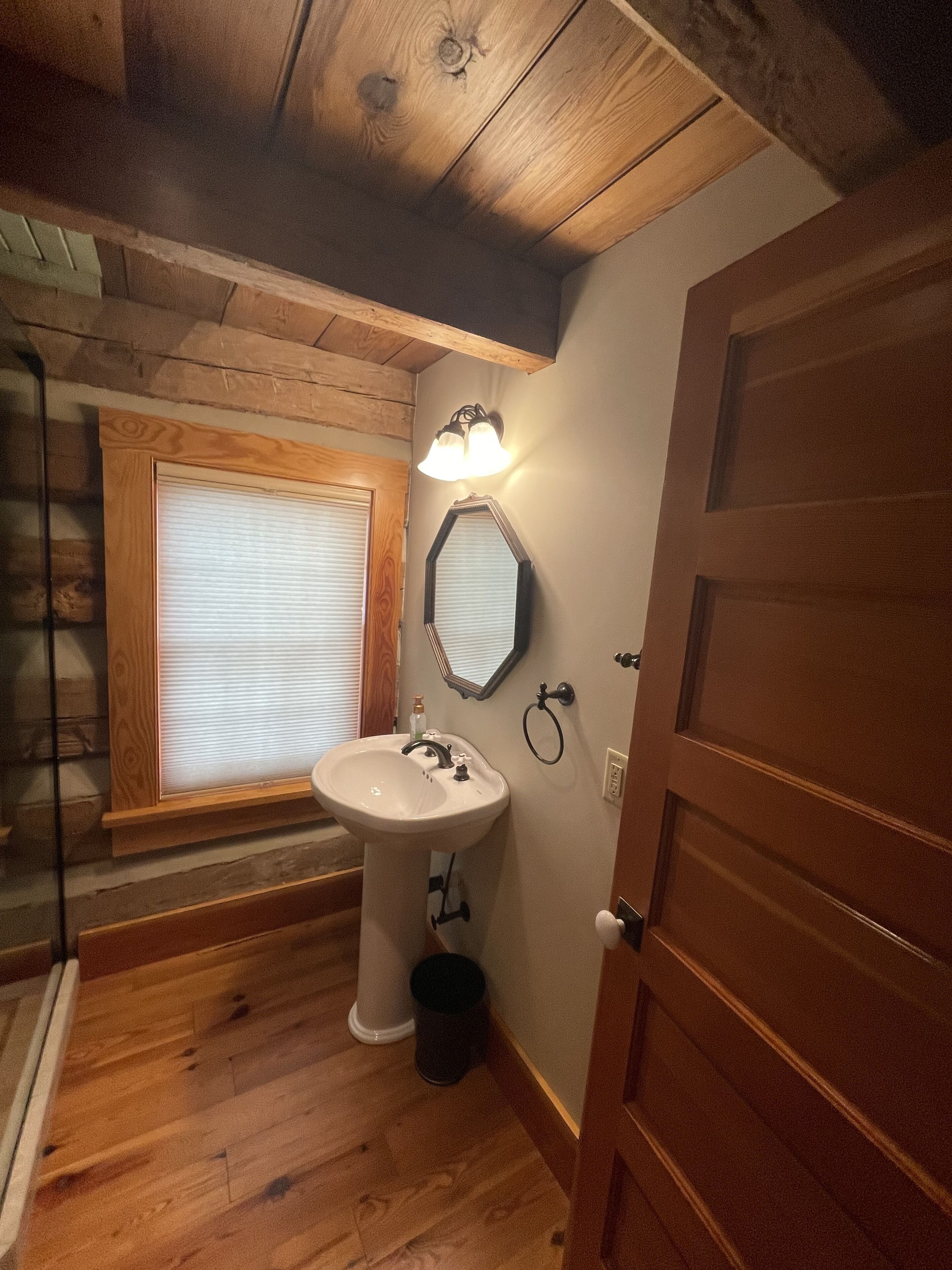 A bathroom with a wooden floor, a white sink, a mirror, and a door.