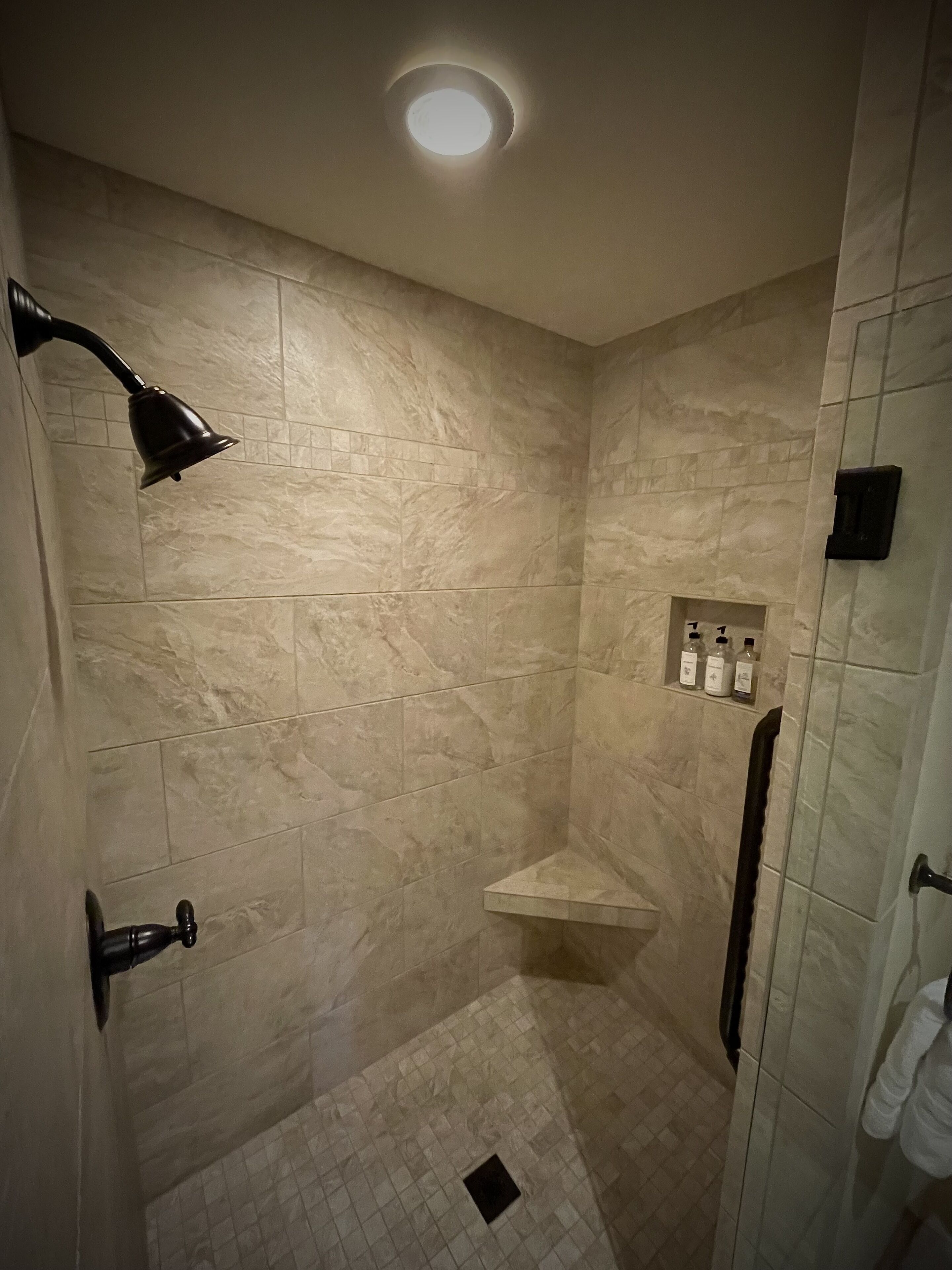 A small, tiled shower with a wall-mounted shelf holding toiletries.