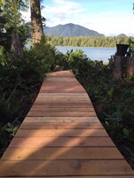 Un sendero de madera que conduce a un lago con montañas al fondo.