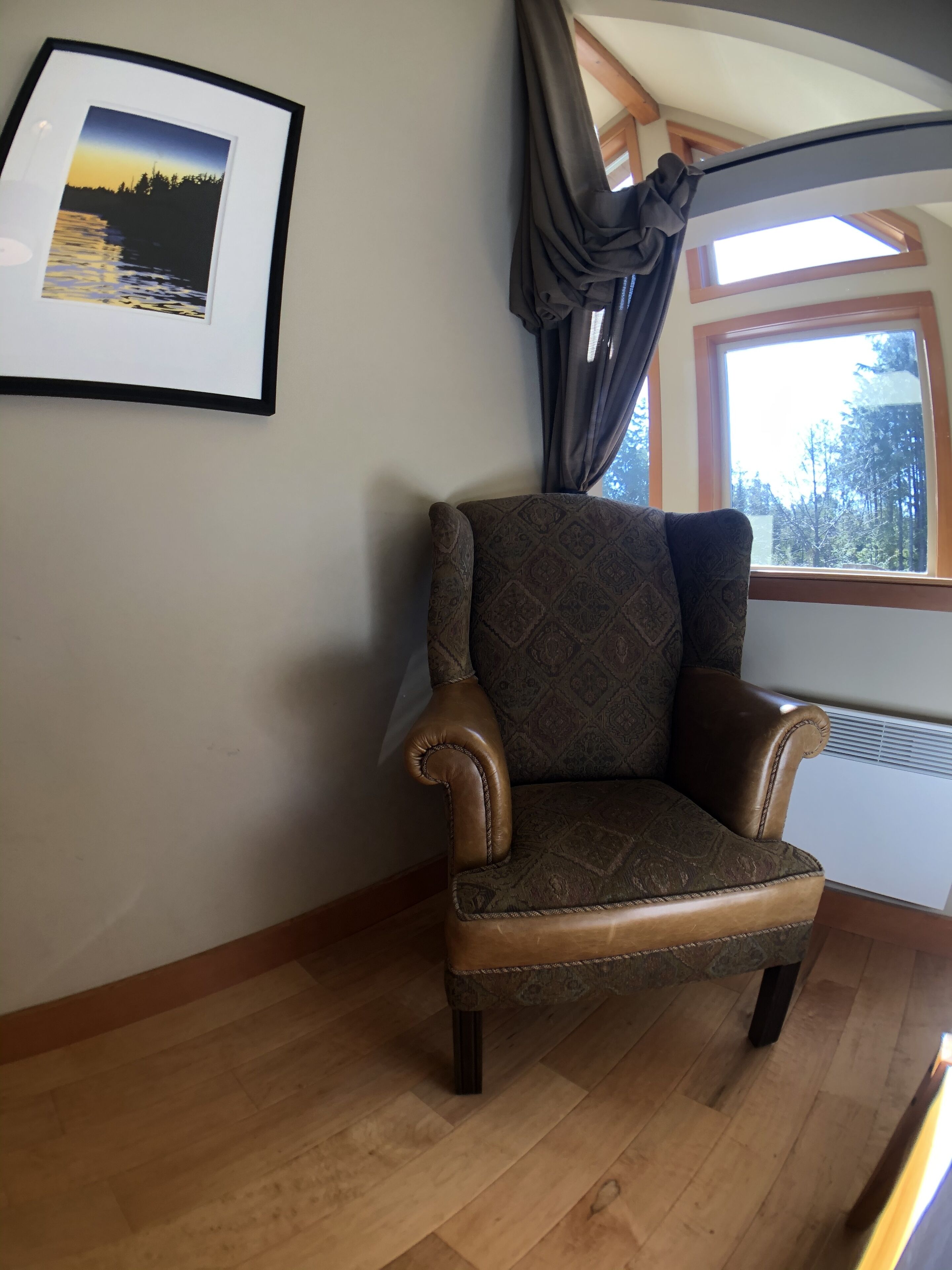 A corner room with a brown leather armchair, a framed picture on the wall, and a window with curtains.