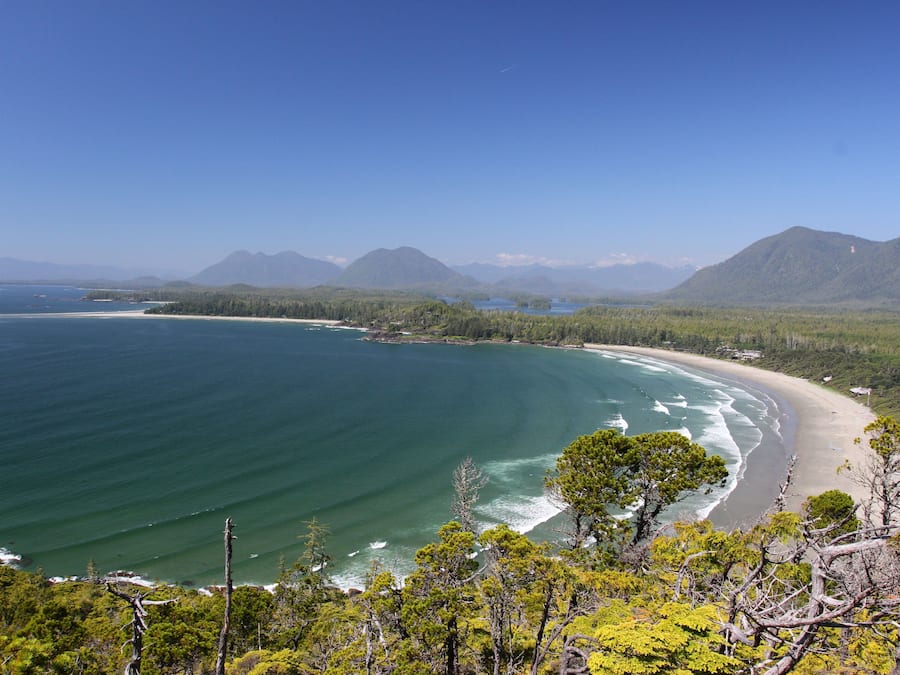 A coastal landscape with a beach, clear blue waters, and surrounding mountains.