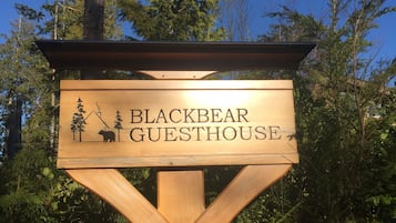 A wooden sign for Black Bear Guesthouse with a bear illustration and trees.