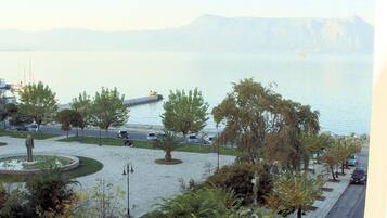 A waterfront parking area with trees and a fountain, overlooking a calm body of water with mountains in the distance.