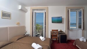 A hotel room with two beds, a TV, a desk, a chair, and a balcony with a view. - Konstantinoupolis Hotel - Adults friendly (Corfu)