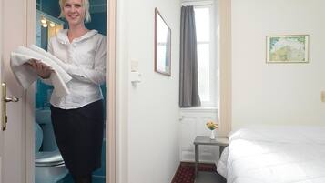 Quarto de hotel com cama, uma mesinha com um vaso de flores, janela com cortinas e um quadro na parede.