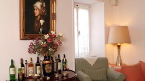 Un salon avec un fauteuil à rayures vertes, une table avec des bouteilles de vin, un vase rempli de fleurs et un tableau accroché au mur.