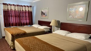 A hotel room with two beds, a wooden headboard, a lamp, and two framed pictures on the wall.