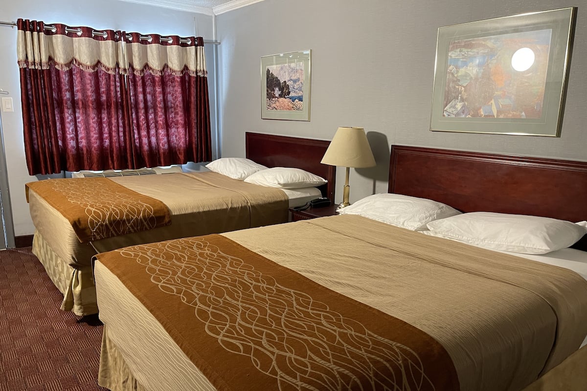 A hotel room with two beds, a wooden headboard, a lamp, and two framed pictures on the wall.