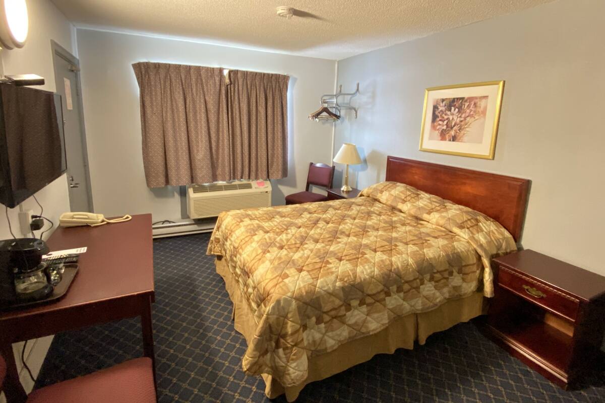 A hotel room with a bed, a desk, a chair, a TV, a lamp, and a framed picture on the wall.