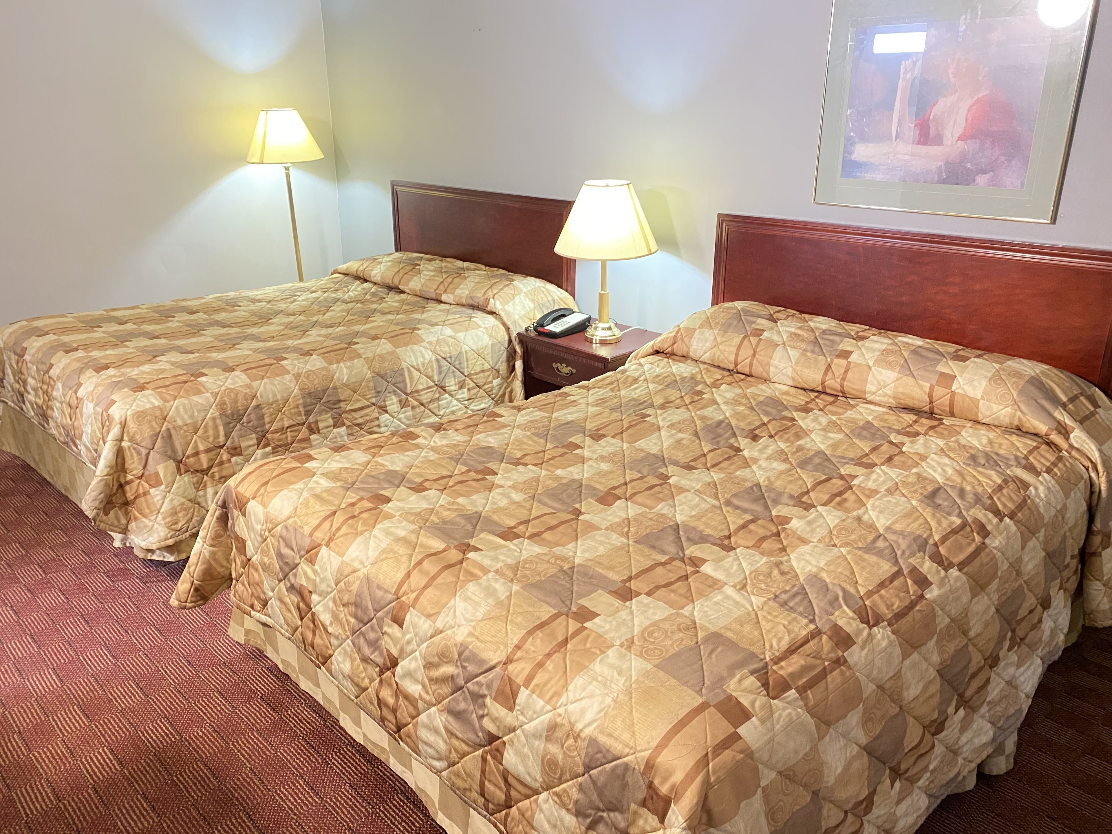A hotel room with two beds, each with a patterned quilt, bedside lamps, and a nightstand with a phone and lamp.