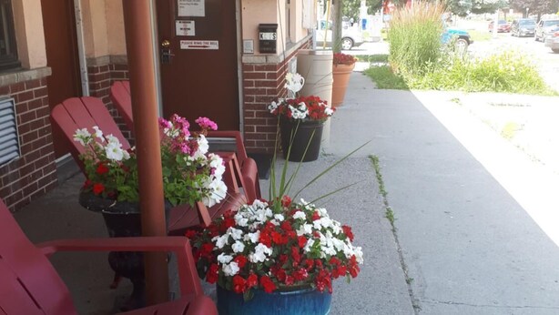 A building with an 'Office Bureau' sign, outdoor seating with red chairs, and a large planter with flowers.