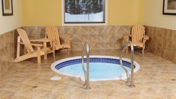 A spa area with a hot tub, wooden chairs, and a window with a snowy view. - Trend Mountain Hotel & Conference Centre (Tumbler Ridge)