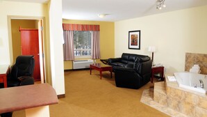A hotel room with a sofa, a desk, a chair, a bed, a bathroom, and a window with curtains. - Trend Mountain Hotel & Conference Centre (Tumbler Ridge)