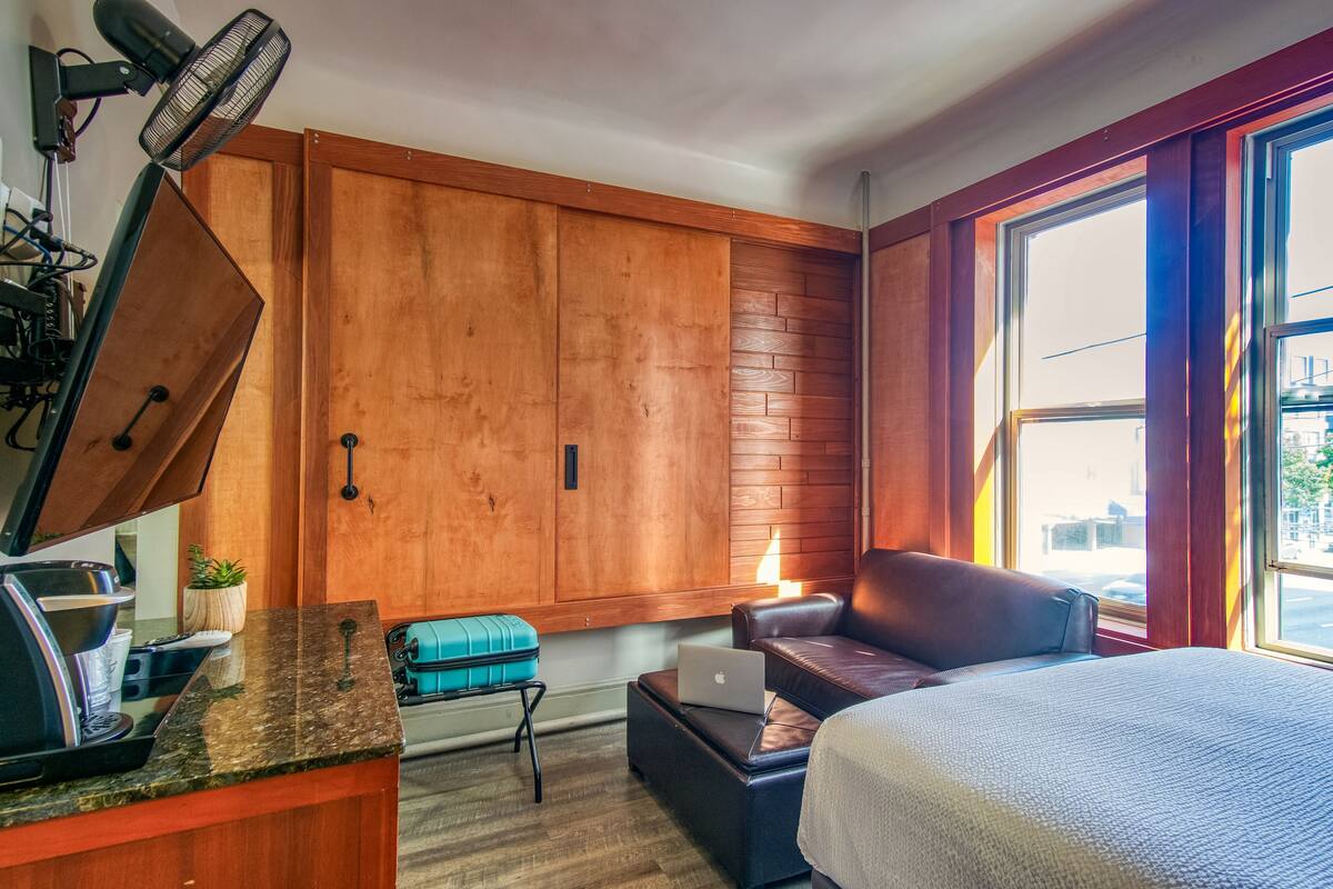 A compact room with a wooden wardrobe, a small kitchenette, a bed, and a window with a view.