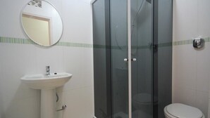 Kylpyhuone, jossa on lasiseinällä varustettu suihku, valkoinen pesuallas ja wc.