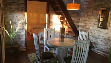 Un interior rústico de madera con una mesa redonda y sillas, una escalera y una lámpara colgante.