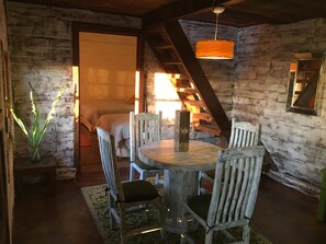 Un interior rústico de madera con una mesa redonda y sillas, una escalera y una lámpara colgante.