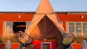 Una tienda de campaña montada frente a un edificio, con dos sillas y una mesa.