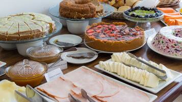 Una mesa de buffet con diversas opciones de comida, como pasteles, bollería y fiambres.