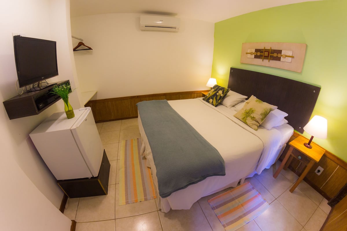 Une chambre d’hôtel bien aménagée, avec un lit, des lampes de chevet, un téléviseur, un petit bureau et un climatiseur fixé au mur.