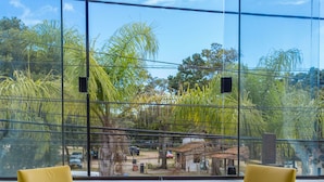 A room with two yellow chairs and a small table, large windows with a view of palm trees and buildings. - Pousada do Centro (Búzios)