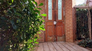 A wooden door with a glass panel, a brick wall, and a wooden deck. - Pousada do Centro (Búzios)