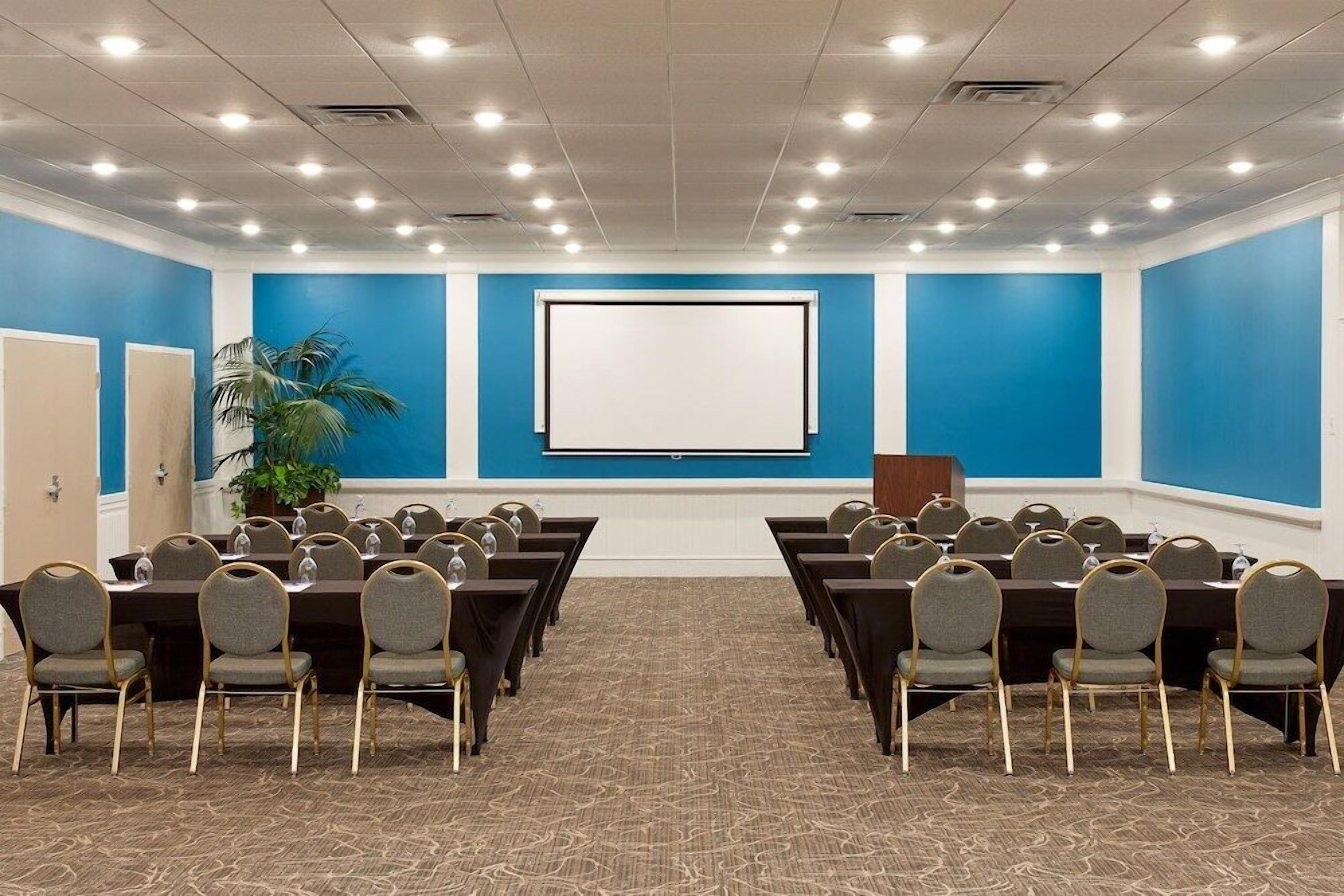 A conference room with a large screen, multiple tables, and chairs arranged for meetings.