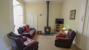 A living room with two leather sofas, a fireplace, a television, and a bookshelf. - Olinda Country Cottages (Olinda)