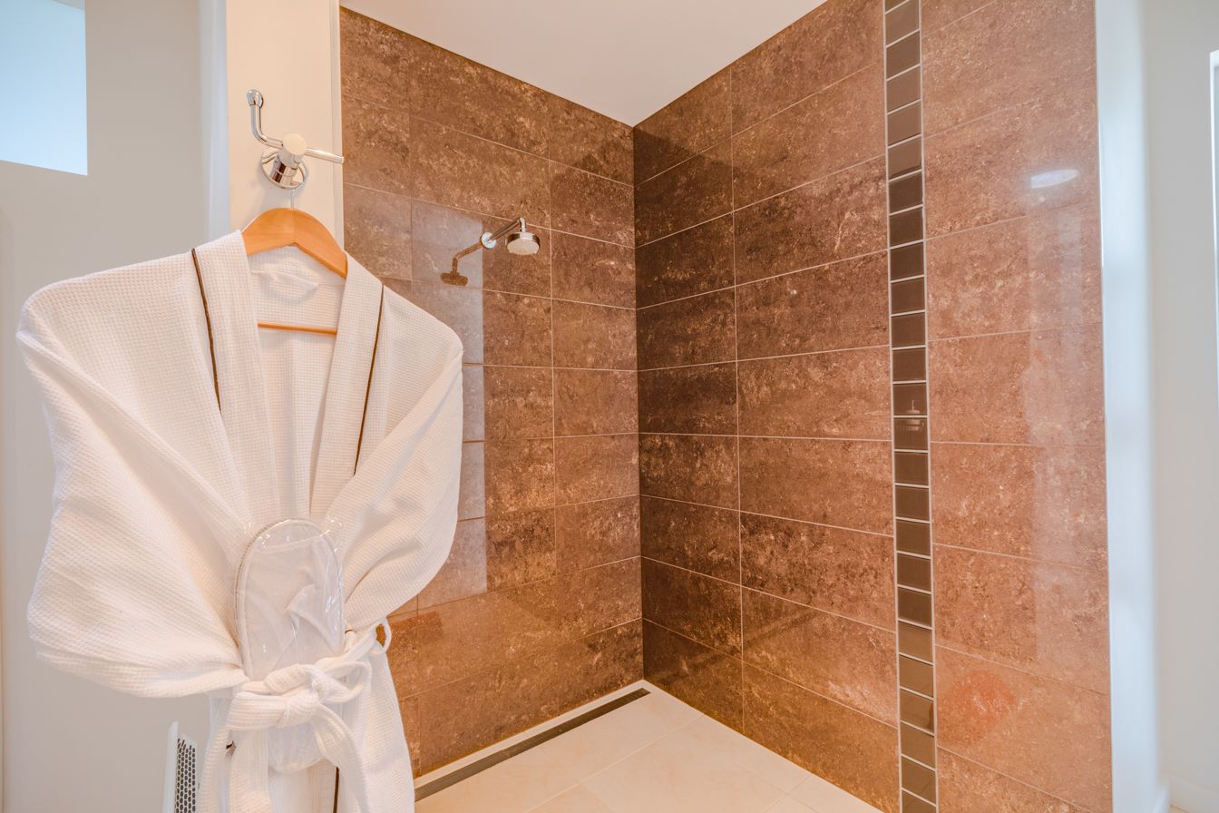 A bathroom with a shower area, a towel rack, and a tiled wall.