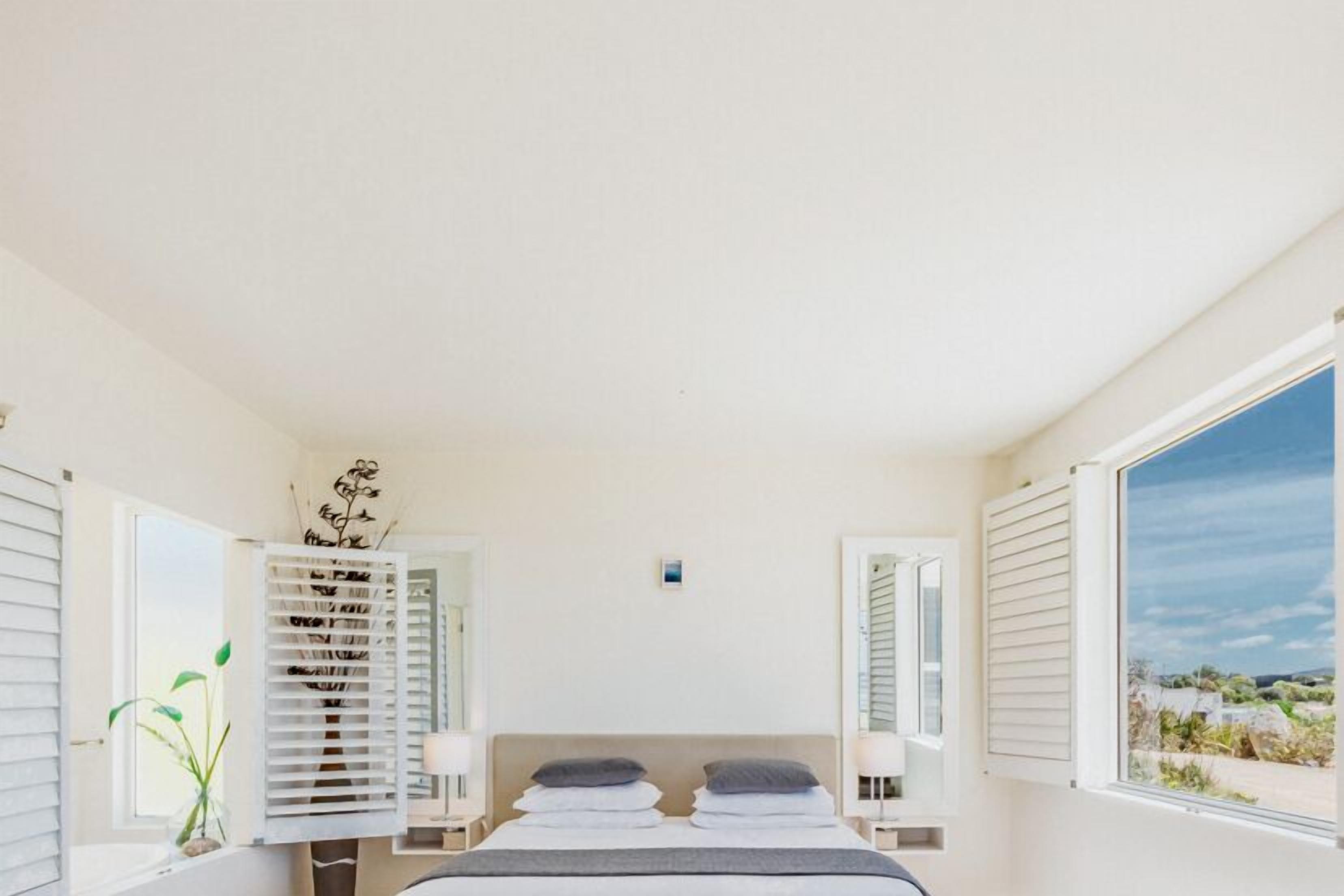A bedroom with a bed, bedside tables, a window with blinds, and a view of the outdoors.
