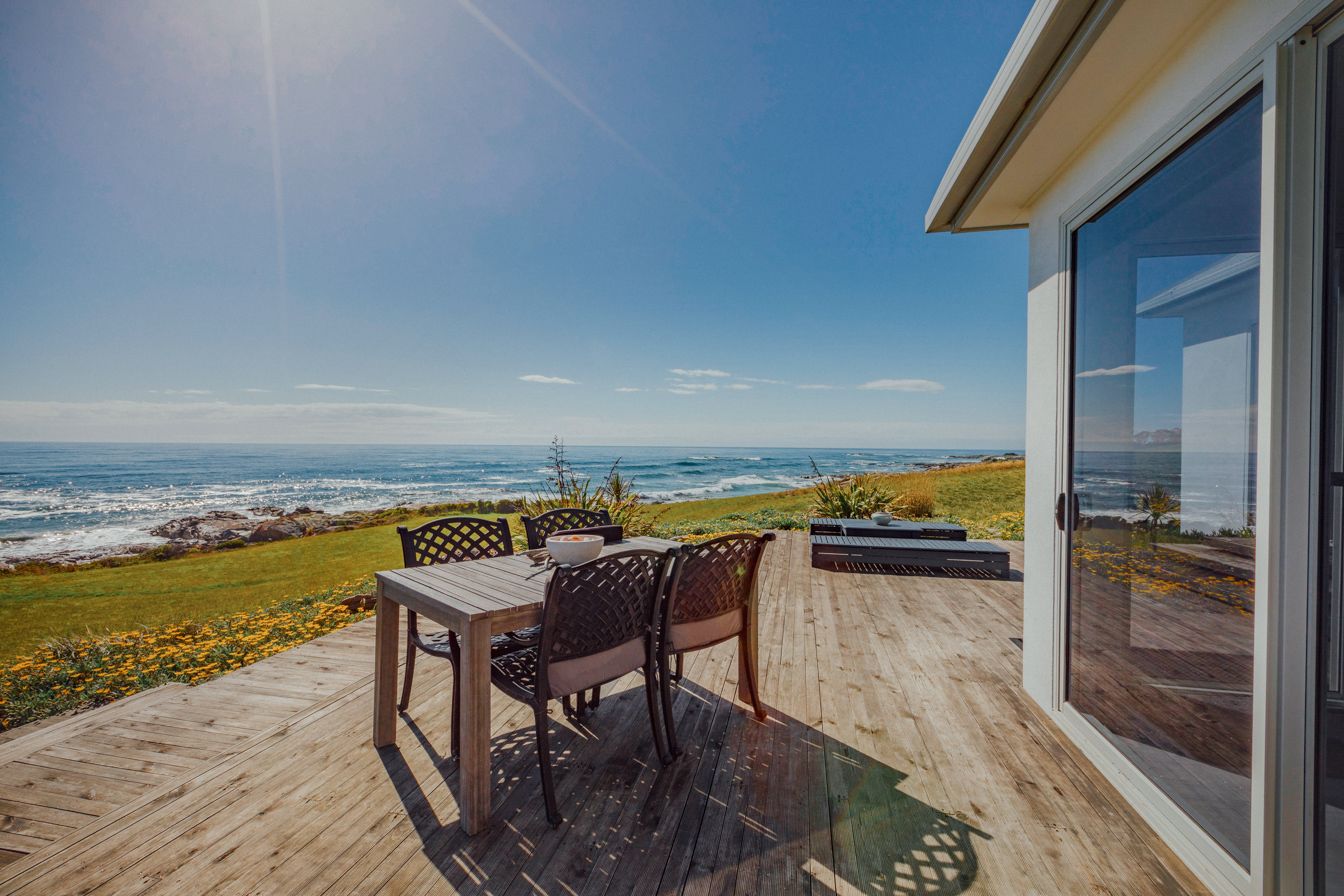 A wooden deck with a table and chairs overlooking the ocean.