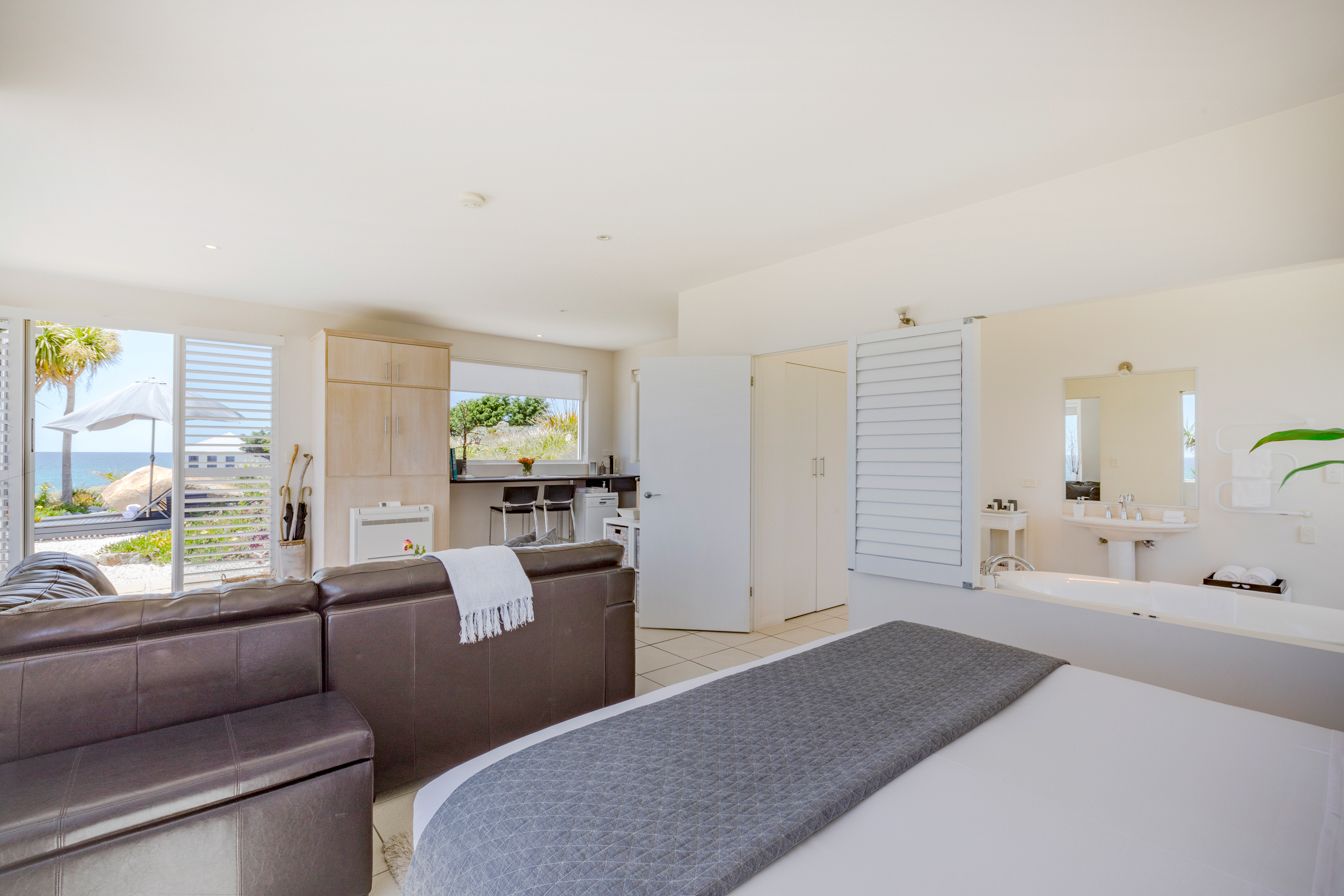 A modern bedroom with a large bed, a sofa, and a view of the beach.