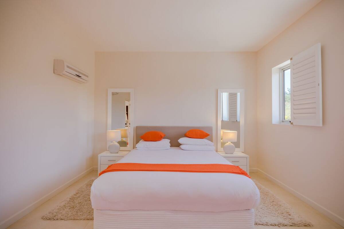 A bedroom with a bed, two nightstands, a mirror, and a window with shutters.