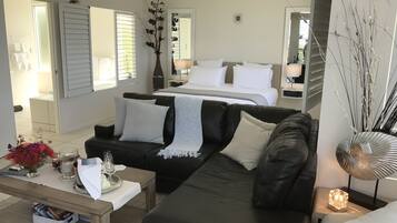 Una habitación de hotel moderna con un sofá de cuero negro, una mesa de centro de madera, una cama con ropa blanca y un espejo grande.