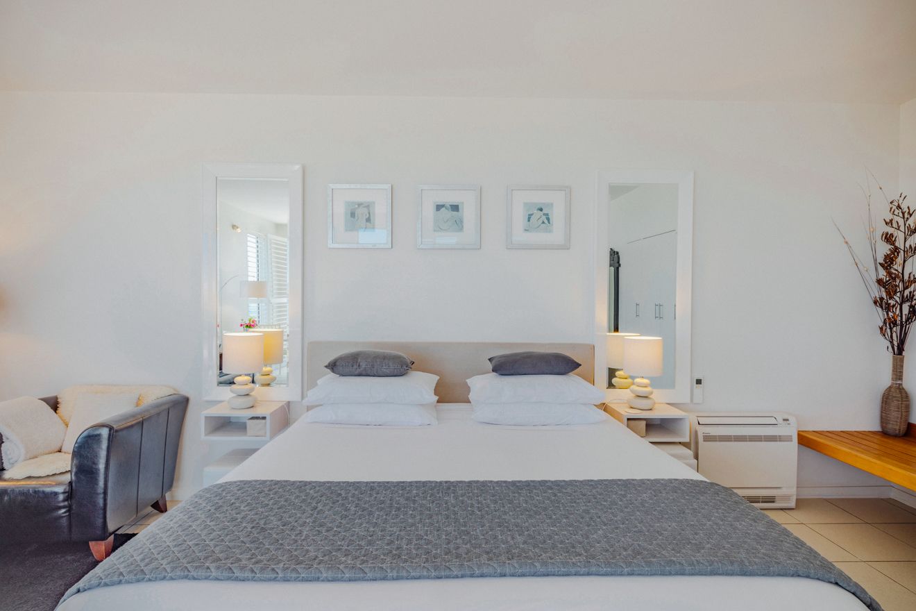 A hotel room with a large bed, two bedside tables with lamps, a chair, a mirror, and framed pictures on the wall.